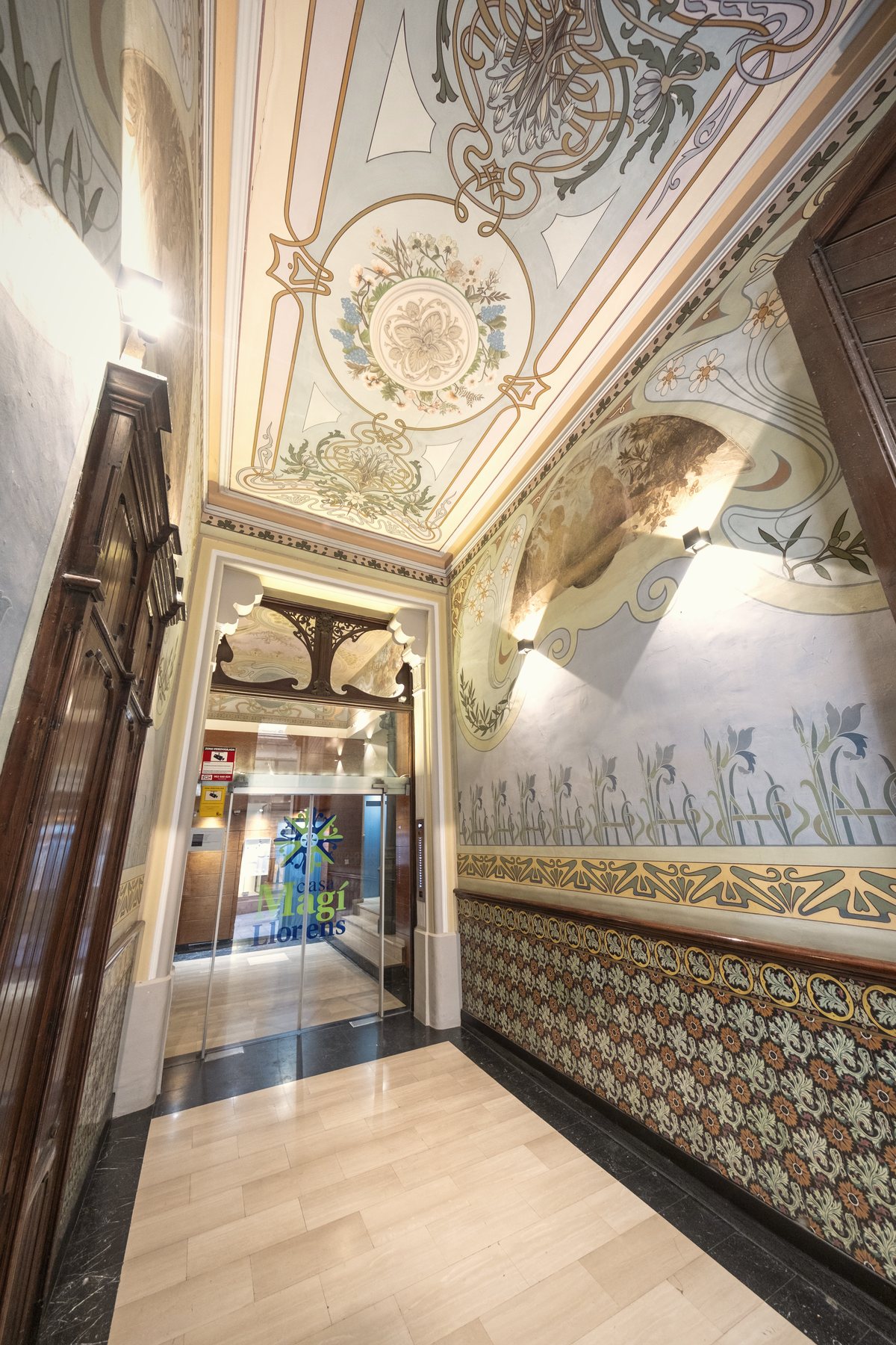 Vestíbul modernista de l'edifici amb el sostre pintat i l'arrimador de rajola